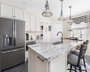 Image of kitchen with white granite countertops and black backsplash tiling with sunshine coming through window